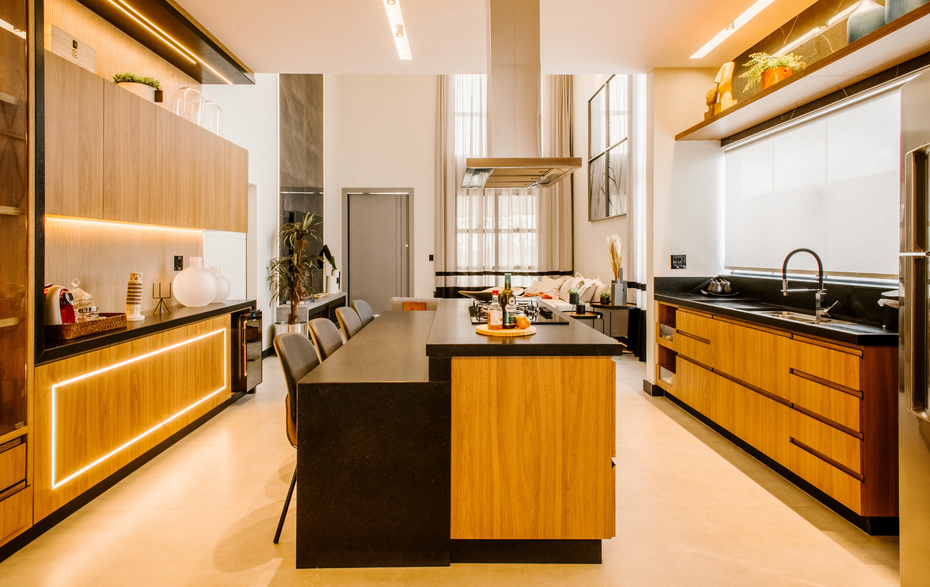 Modern kitchen interior with wood cabinets, black countertops, and a central island under warm lighting