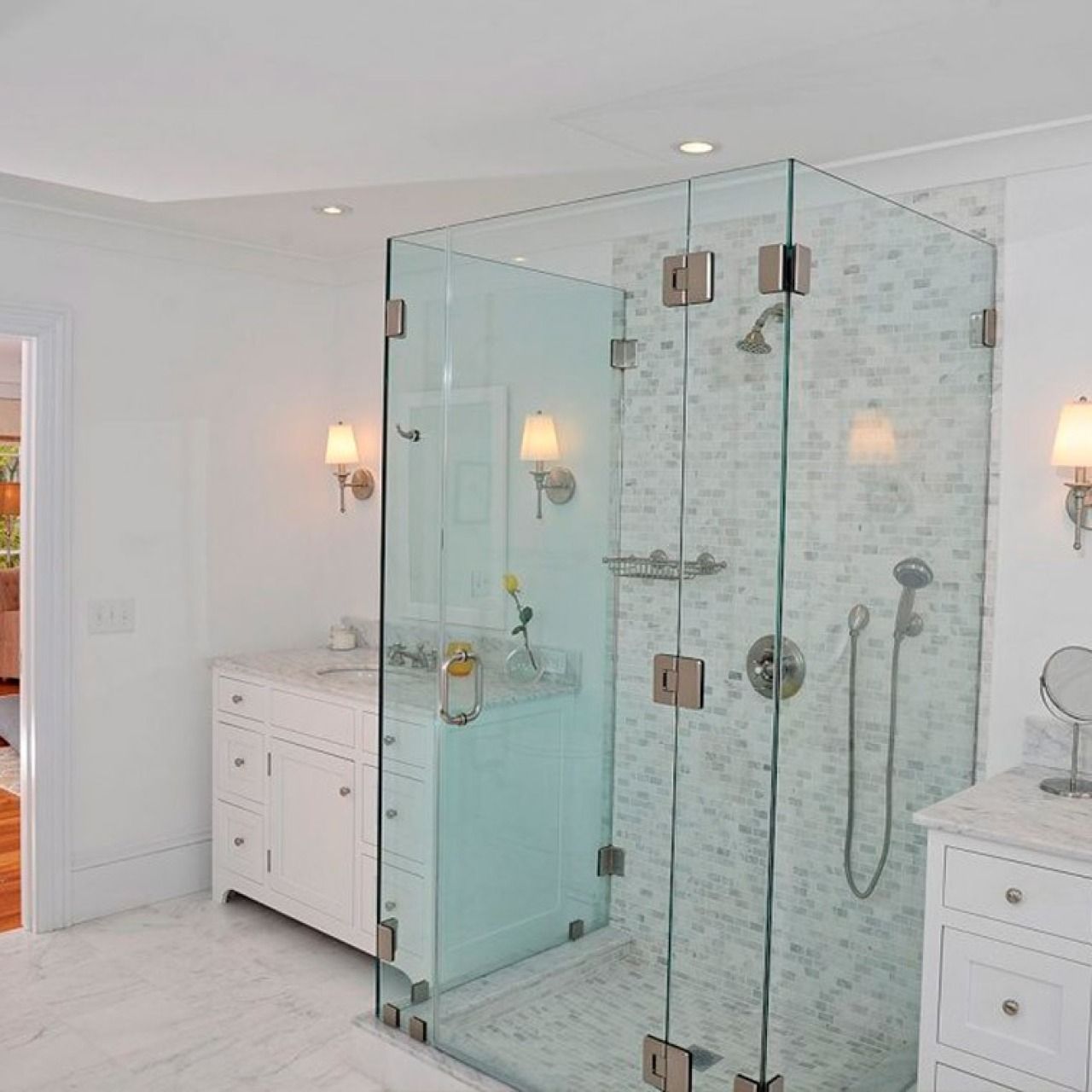 Modern bathroom with a glass walk-in shower, white vanities, and wall sconces