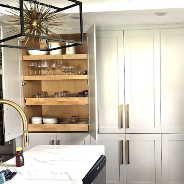 Modern kitchen with white cabinets, wood shelving, marble island, and brass accents