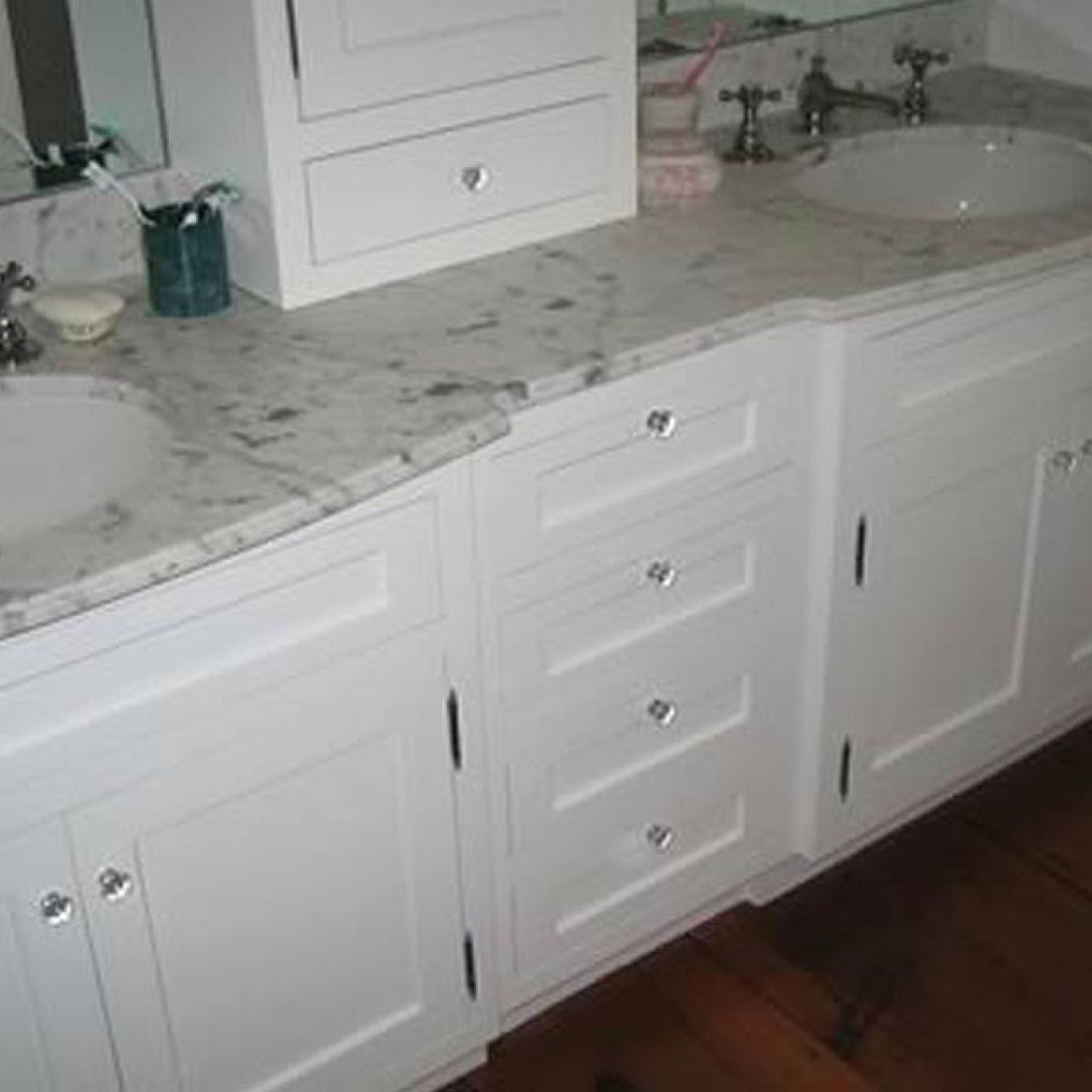 White bathroom vanity with marble countertop, double sinks, and center drawers above a hardwood floor