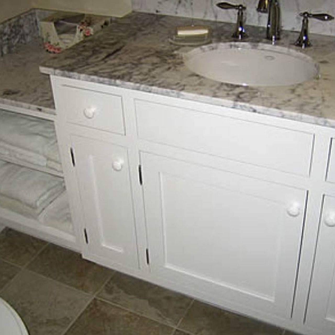 White bathroom vanity with marble countertop, round sink, and built-in open shelving beside it.