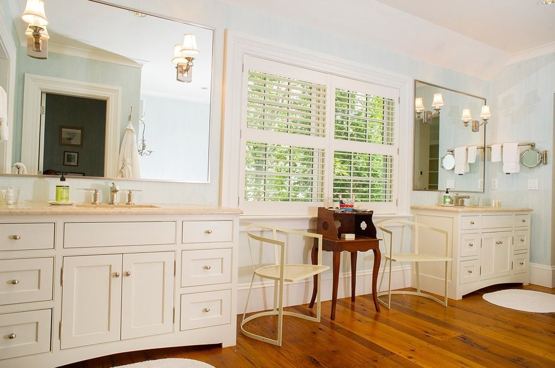 Bright white bathroom with double vanity, large window, mirrors, and hardwood floor