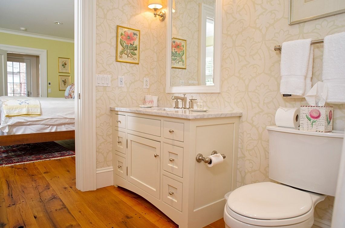 Bright bathroom with white vanity, toilet, towels, and wood floor, viewed from a doorway դեպի bedroom