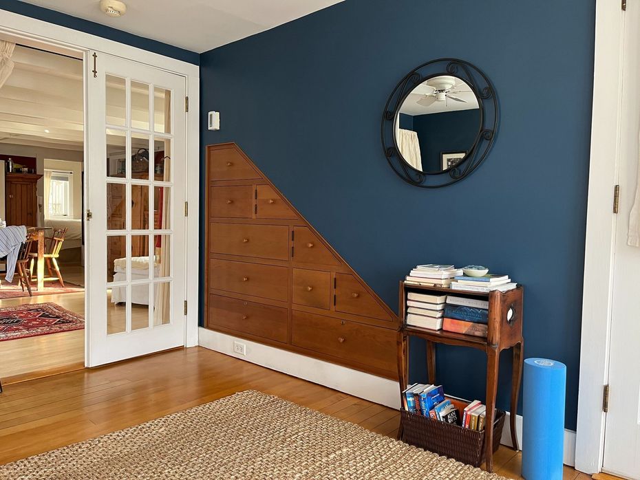 Blue-walled living room corner with a round mirror, wooden stair-front cabinet, and small table beside French doors