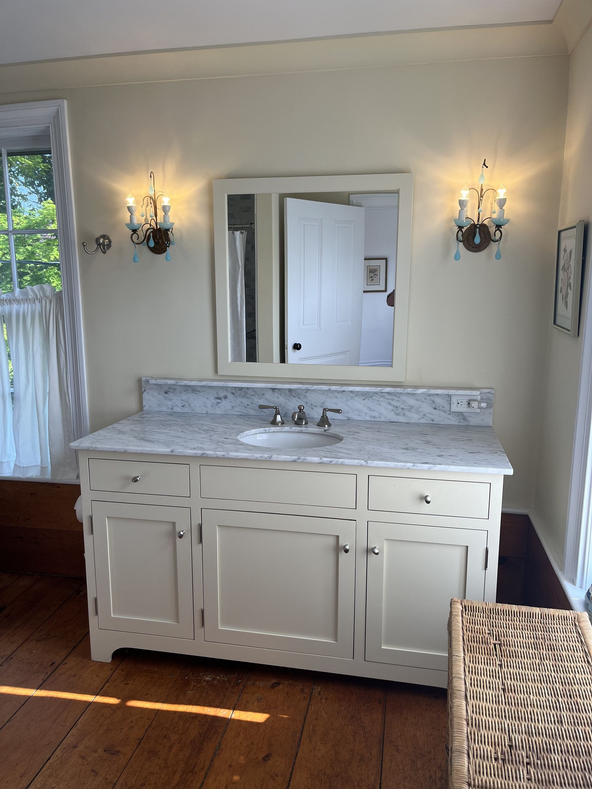 Bathroom vanity with marble countertop, mirror, sconces, and window light in a cream-colored room