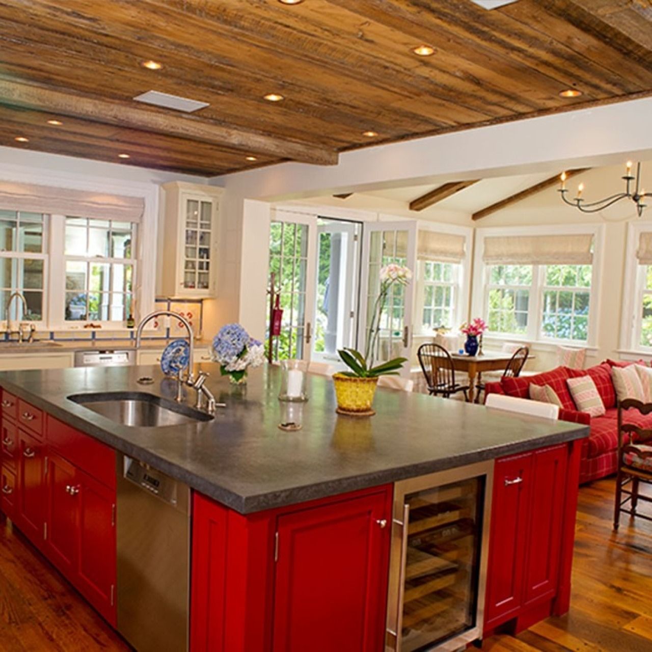Bright kitchen with red island cabinets, wooden ceiling, and a sunlit dining nook
