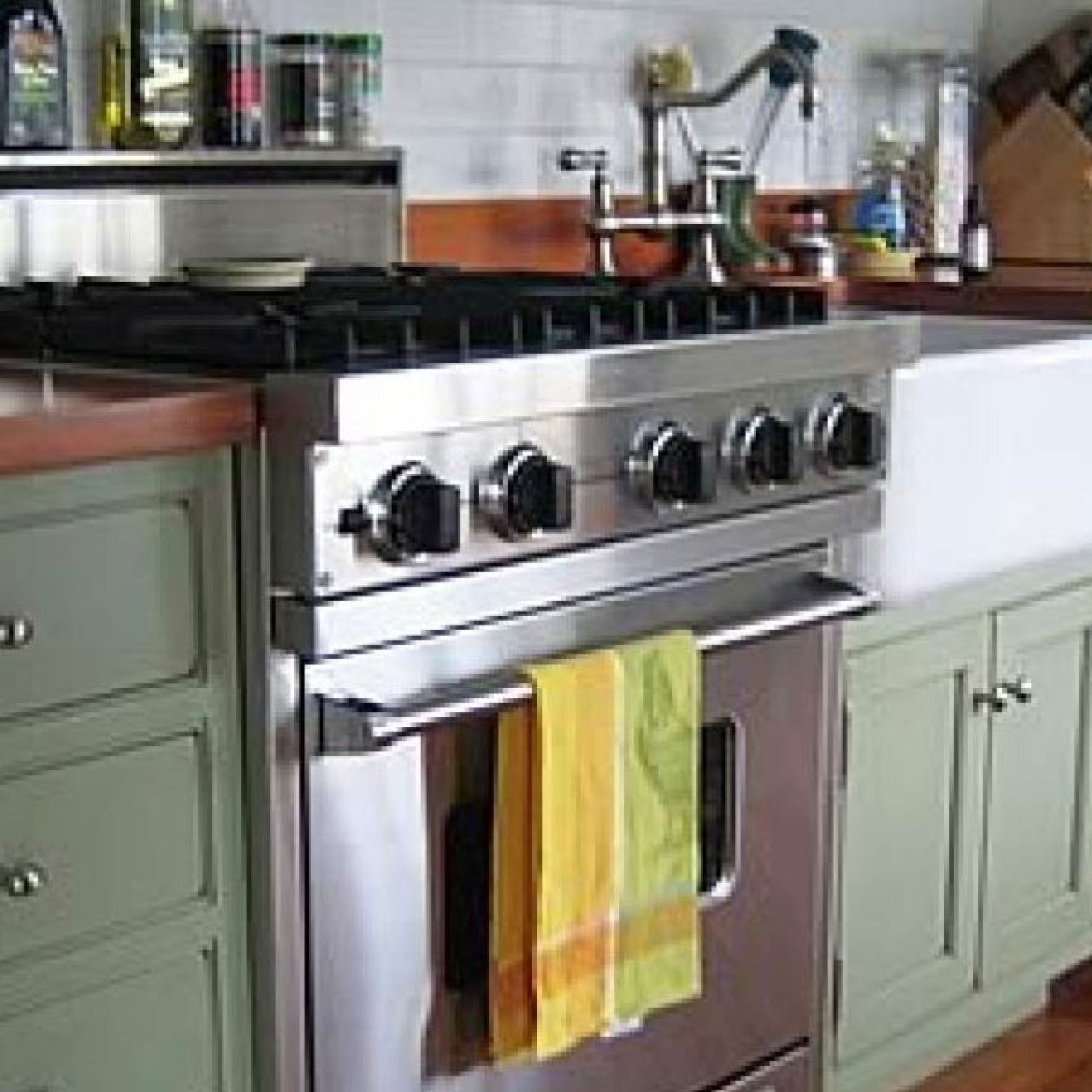 Stainless steel gas stove in a kitchen with green cabinets and a striped towel on the oven door