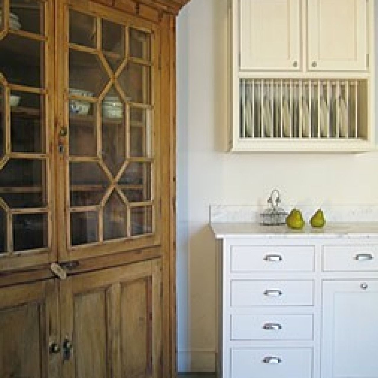 Kitchen with wooden glass cabinet, white cabinets, and two pears on the counter.