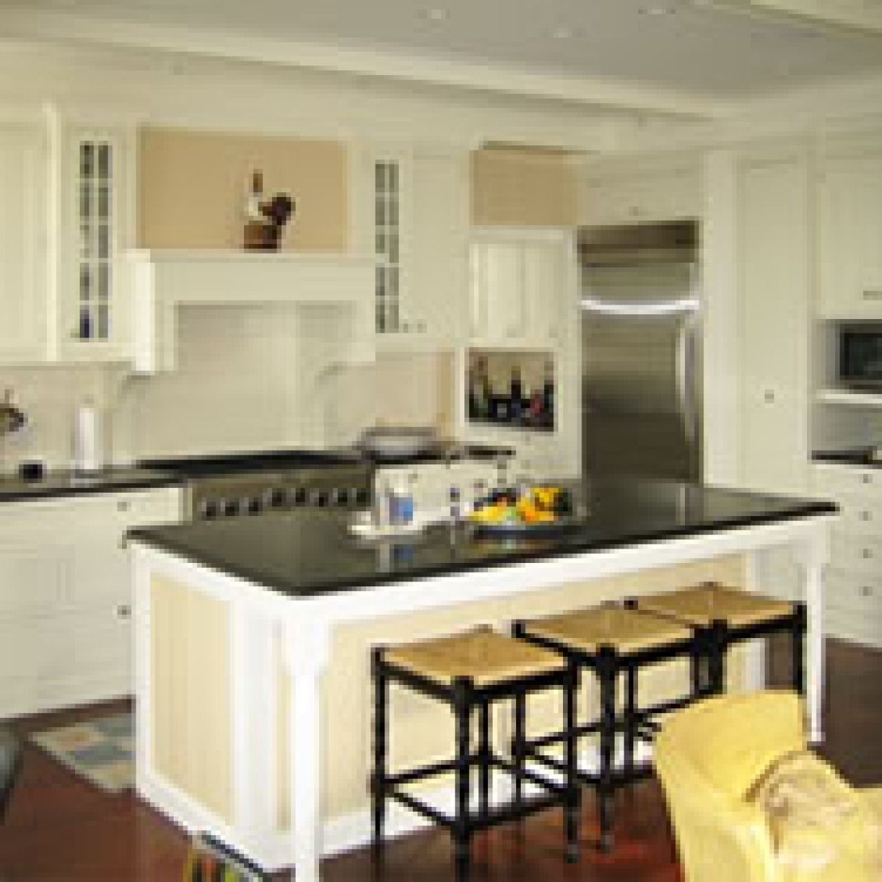 Modern white kitchen with black island, bar stools, stainless steel fridge, and yellow chair