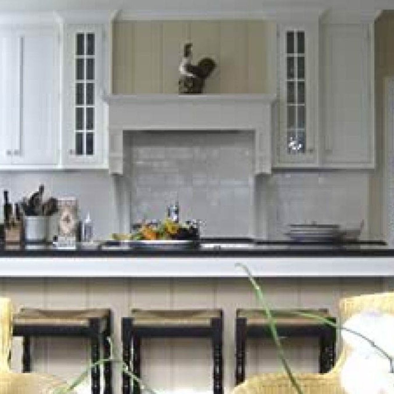 Bright kitchen with white cabinets, black countertop, and three stools at the island.