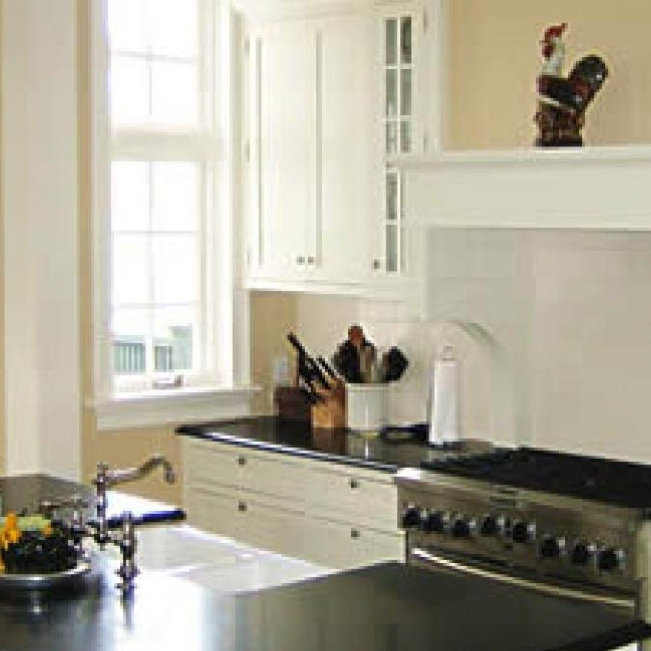 Bright white kitchen with black countertops, stove, sink, and sunlit window.