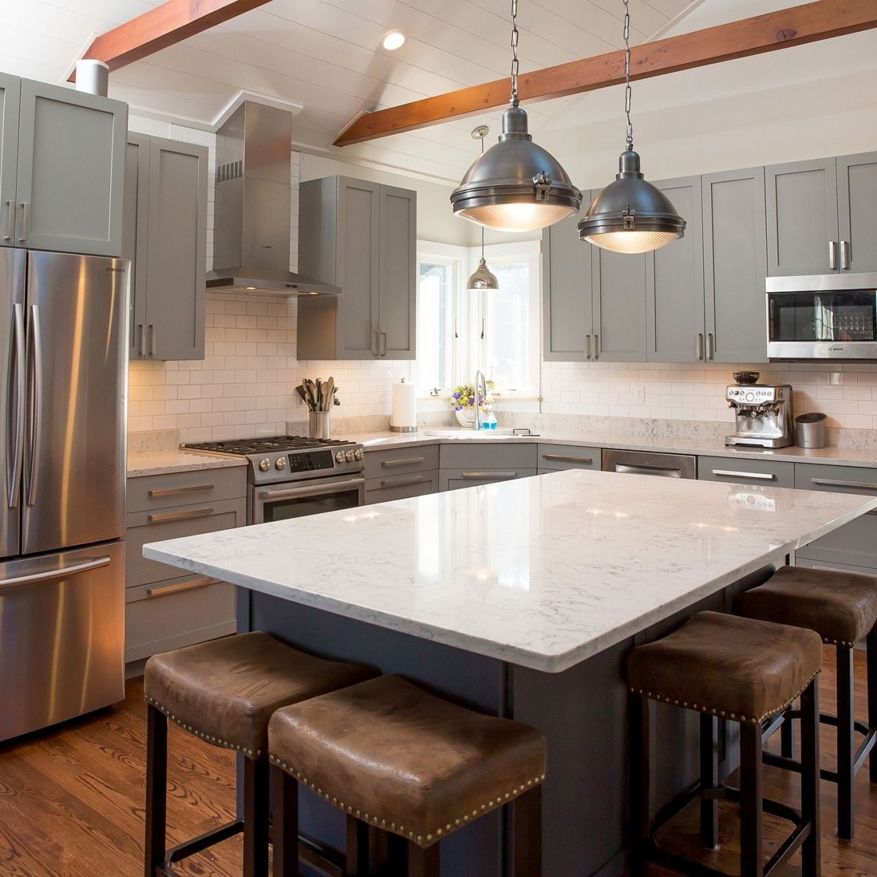 Modern kitchen with gray cabinets, stainless steel appliances, and a large white island with stools