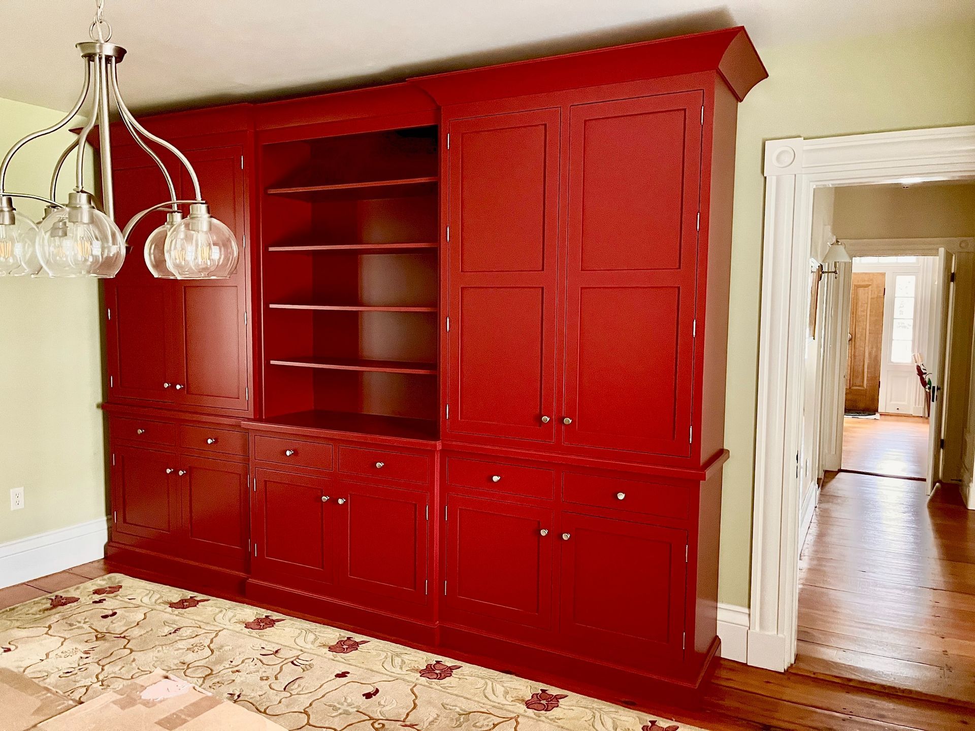 Red built-in wall cabinet with shelves in a beige room, beside a doorway to a hall