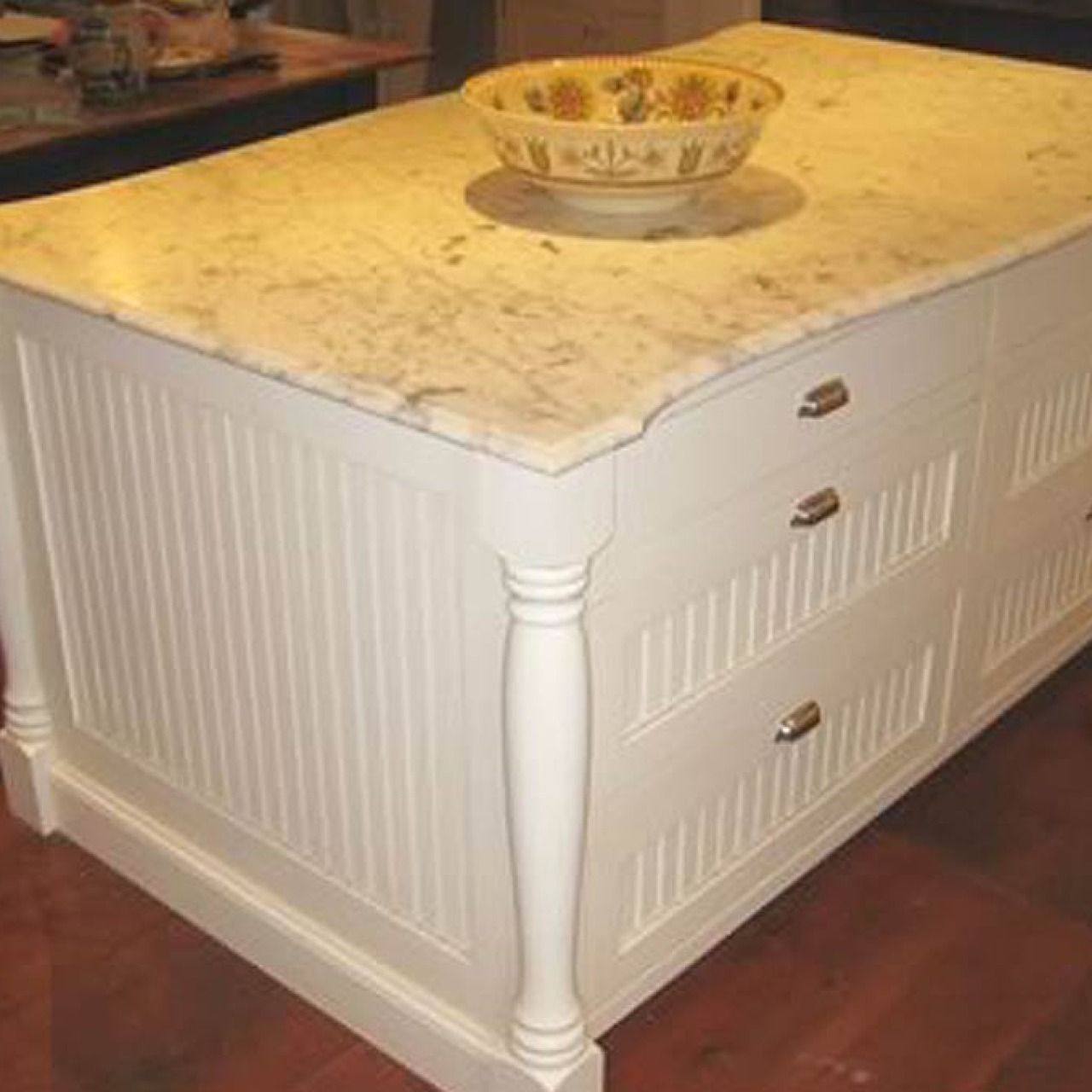 White kitchen island with marble countertop and decorative bowl on top, viewed from the corner