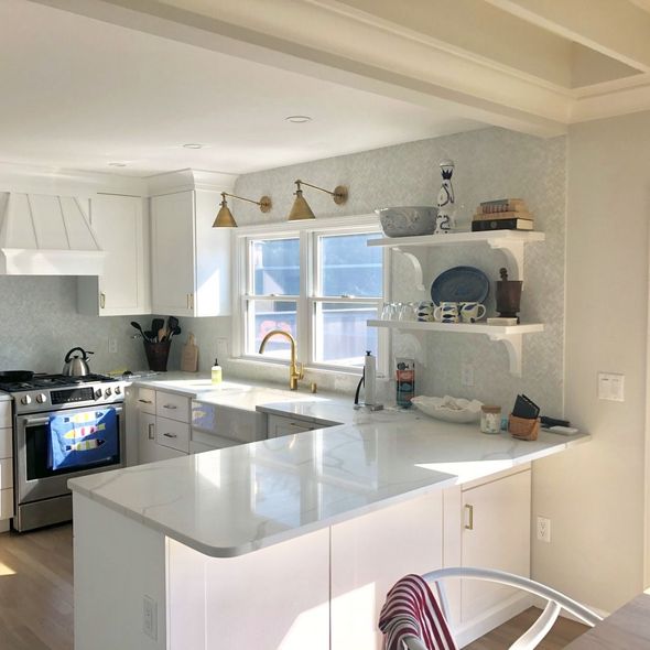Bright white kitchen with island, brass faucet, open shelves, and a sunlit window above the sink