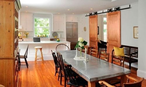 Modern dining room with a long table, black chairs, and a kitchen with wooden floors.