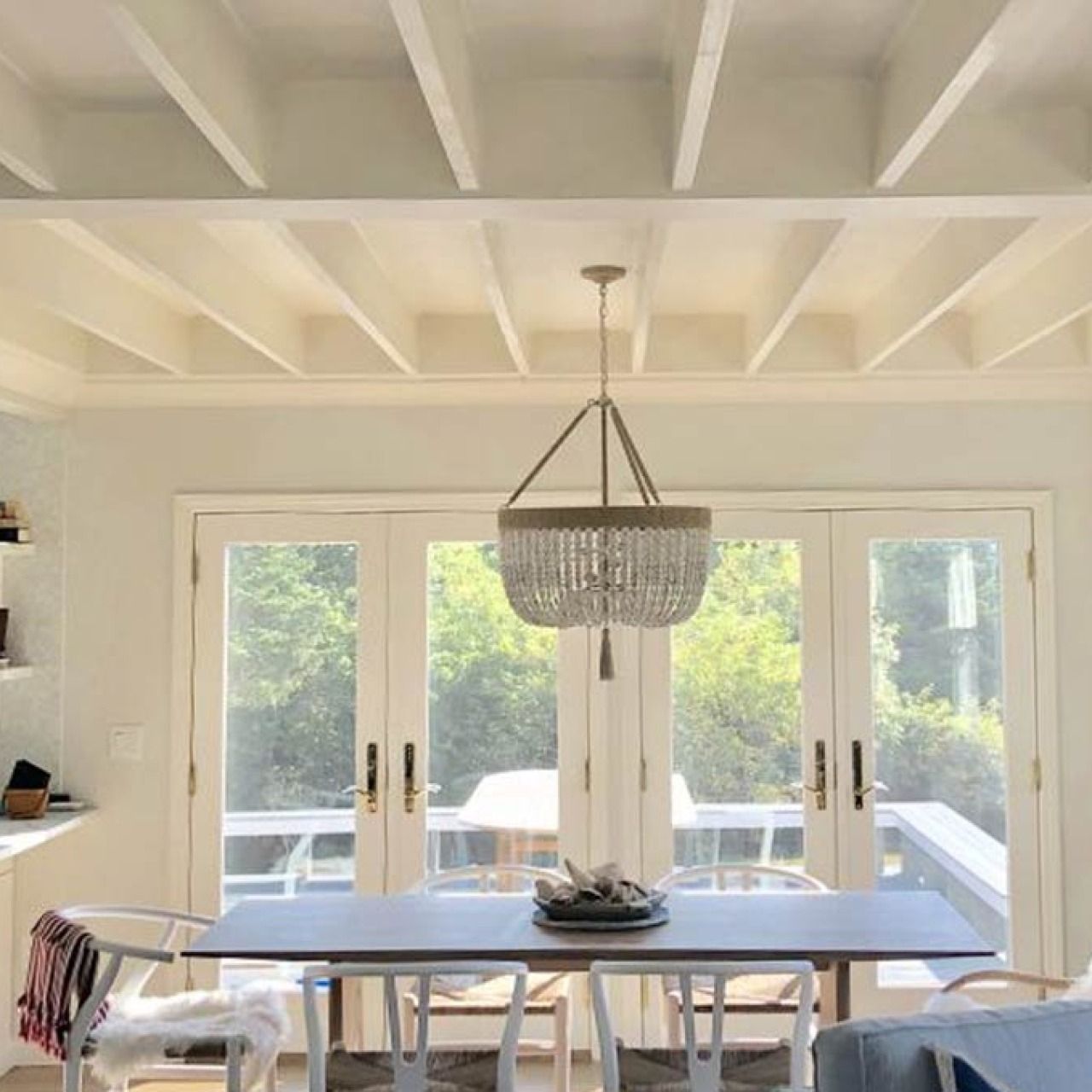 Bright dining room with large windows, white table, wooden chairs, and a hanging chandelier
