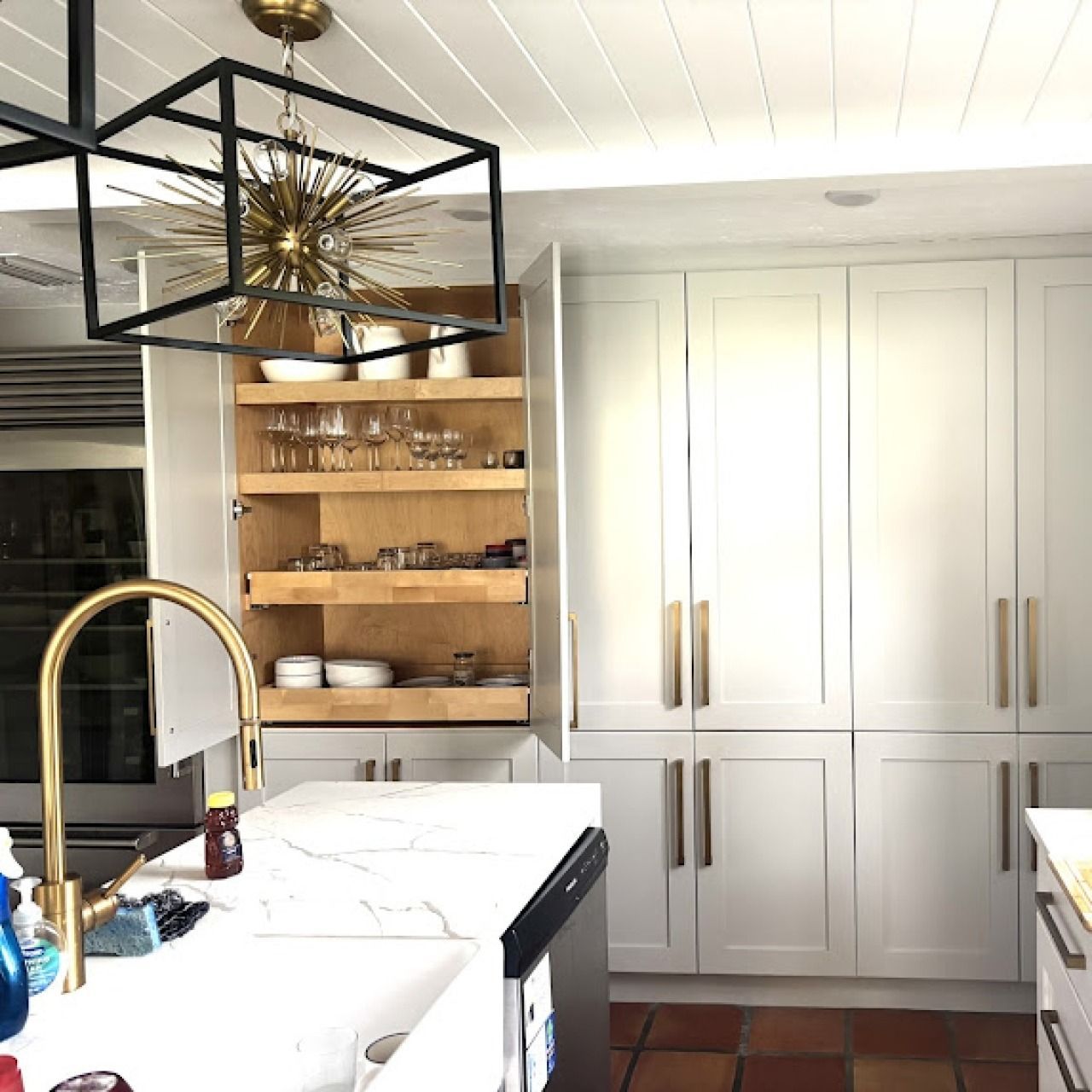 Bright modern kitchen with white cabinets, marble island, brass faucet, and open wood shelving