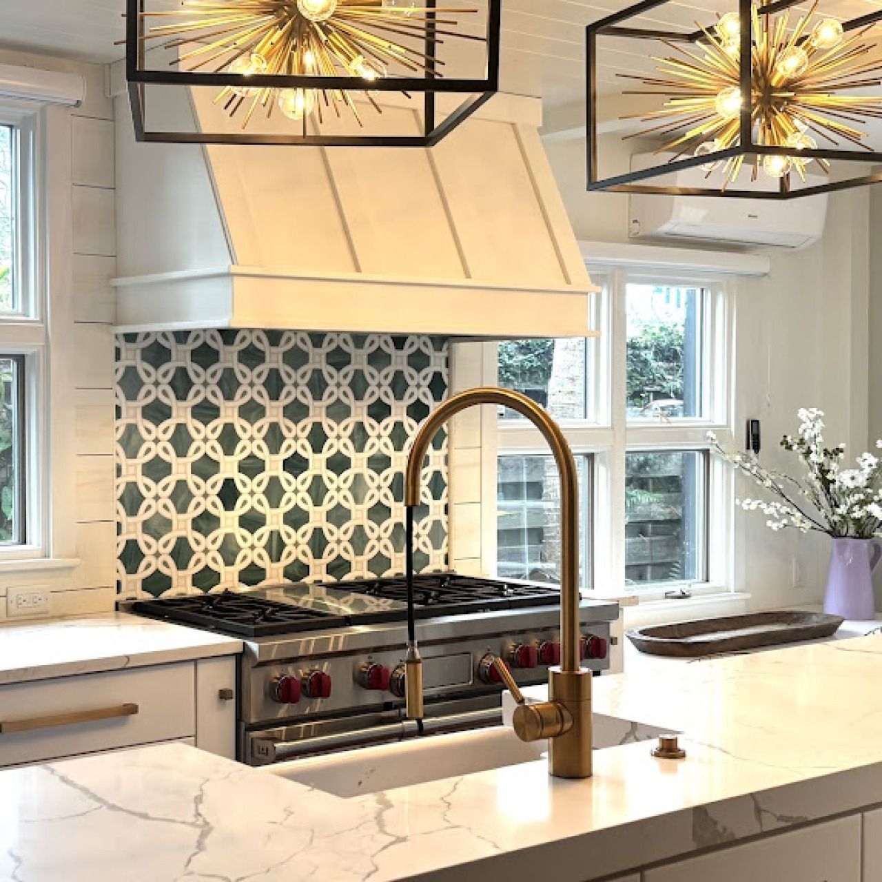 Modern kitchen with white cabinets, blue patterned backsplash, marble island, and brass fixtures