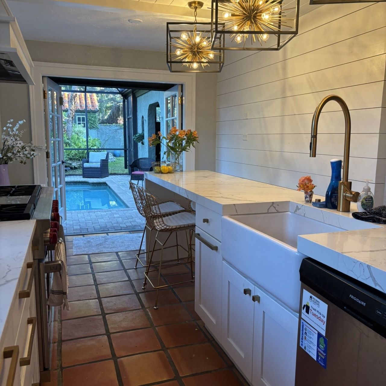 Modern kitchen with white cabinets, terracotta floor, pendant lights, and open doors to a sunny patio