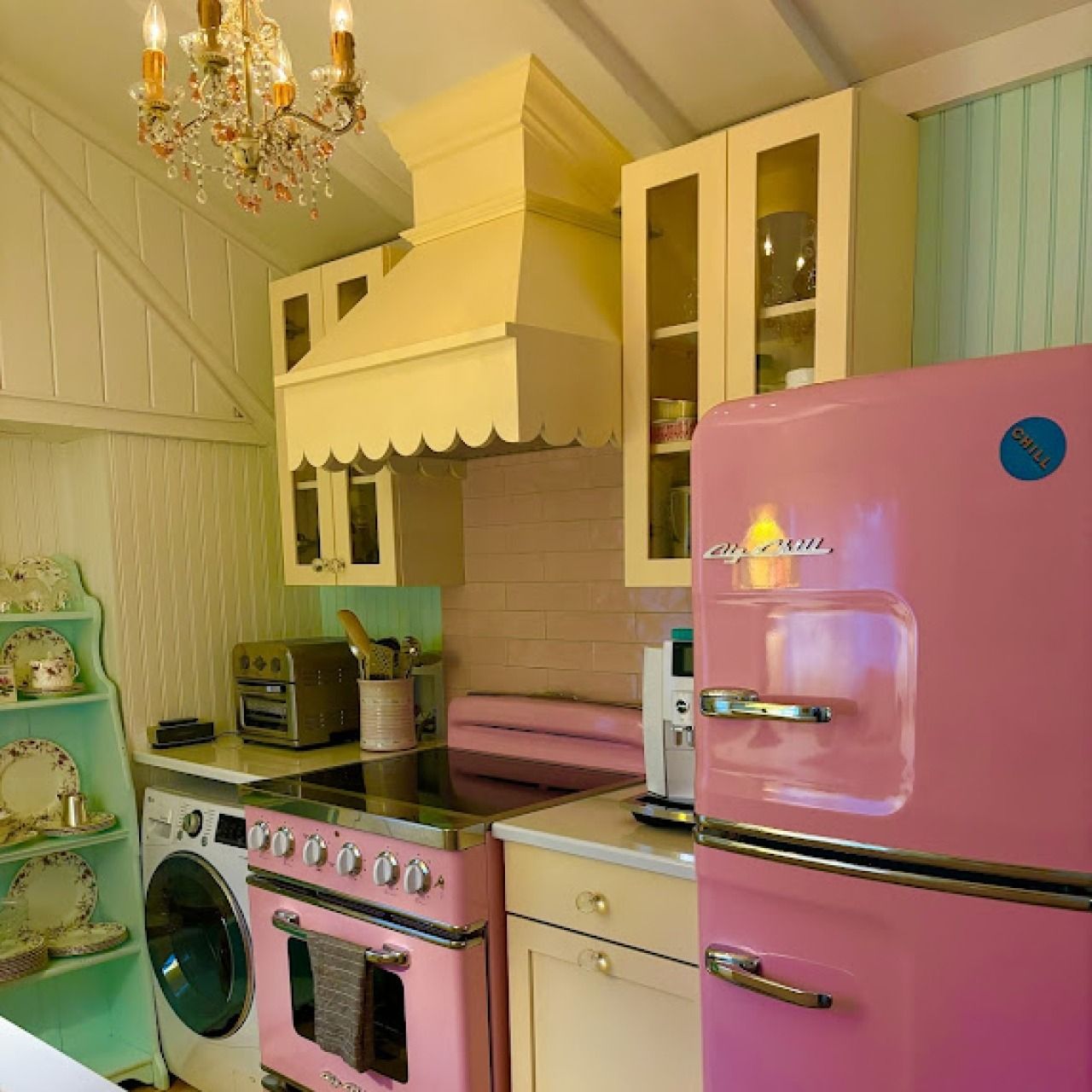 Pink retro kitchen with vintage stove, mint washer, chandelier, and glossy refrigerator