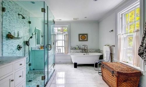 Bright bathroom with glass shower, freestanding tub, white tile, and wicker basket by the window.