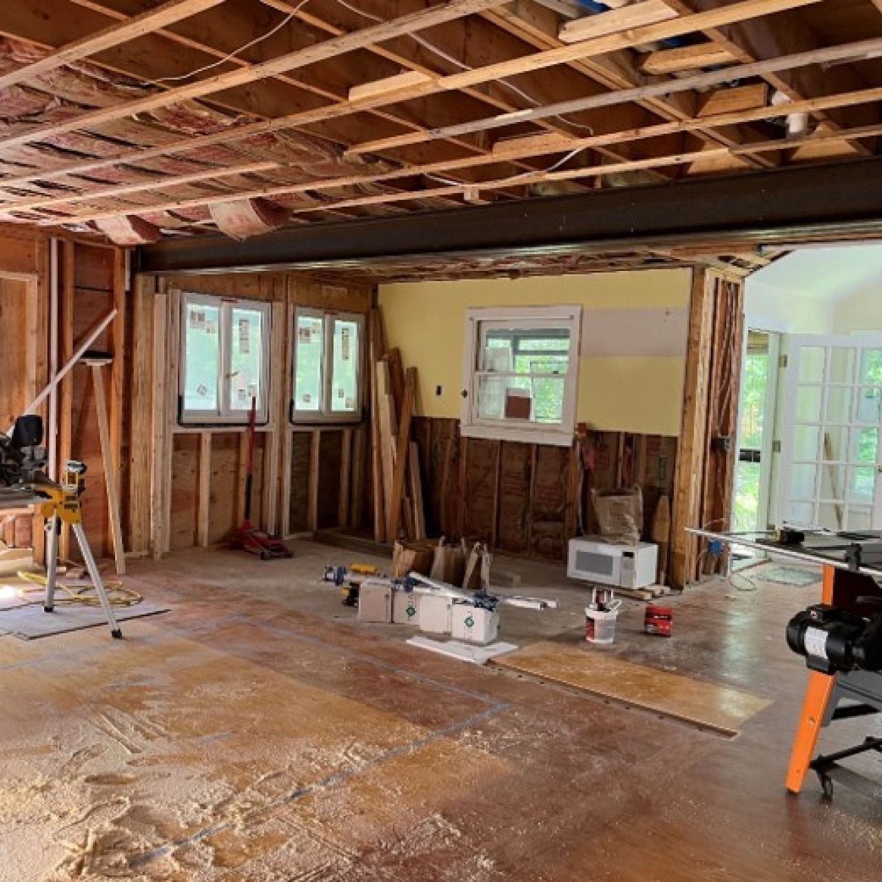 Interior of a house under renovation, with exposed studs, unfinished ceiling, tools, and debris on the floor.