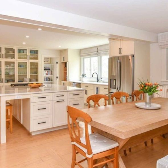 Bright modern kitchen with white cabinets, island, wooden dining table, and large windows