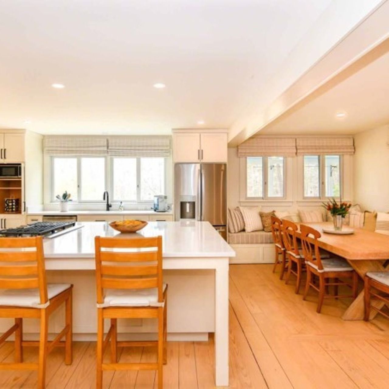Bright modern kitchen and dining area with white island, wooden chairs, and large windows