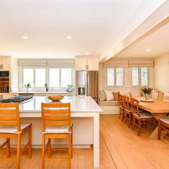 Bright modern kitchen and dining area with white island, wooden chairs, and large windows