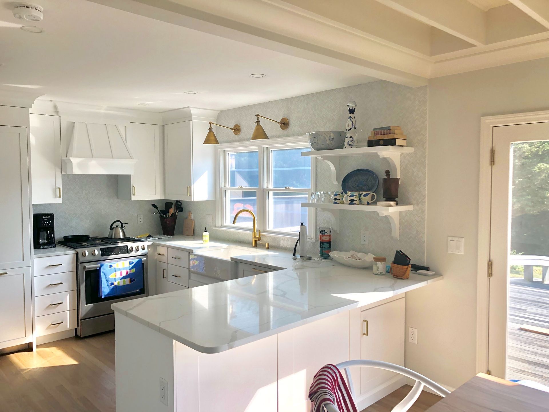 Bright white kitchen with island, gray countertops, blue cabinets, and a sunlit window over the sink