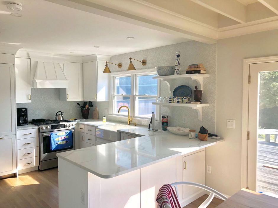 Bright white kitchen with island, gray countertops, blue cabinets, and a sunlit window over the sink