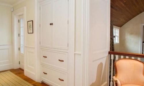 Bright hallway with white built-in cabinets, wood floor, and a peach chair beside an open room.