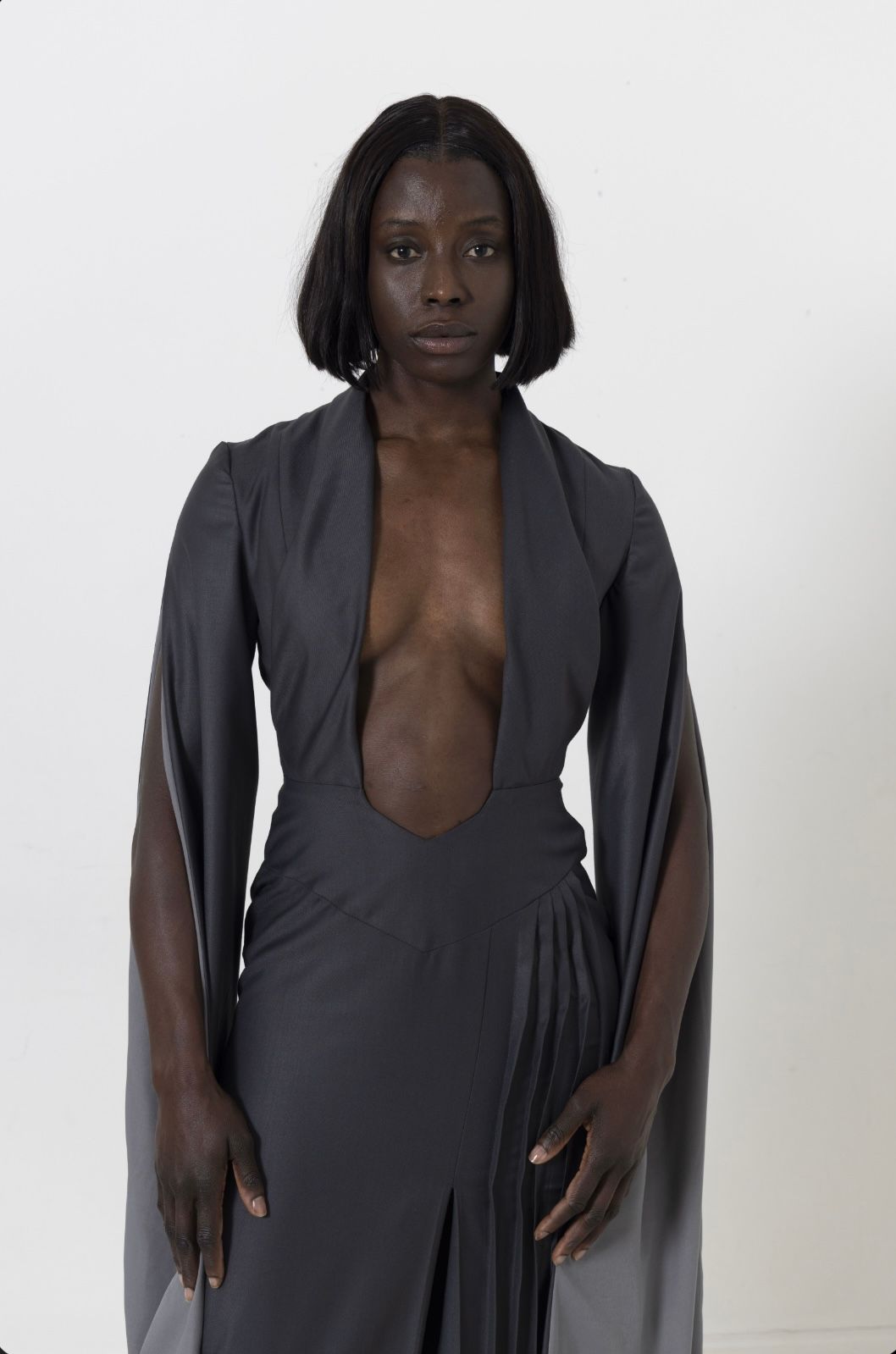 Woman in a gray, plunging neckline dress poses against a white backdrop.
