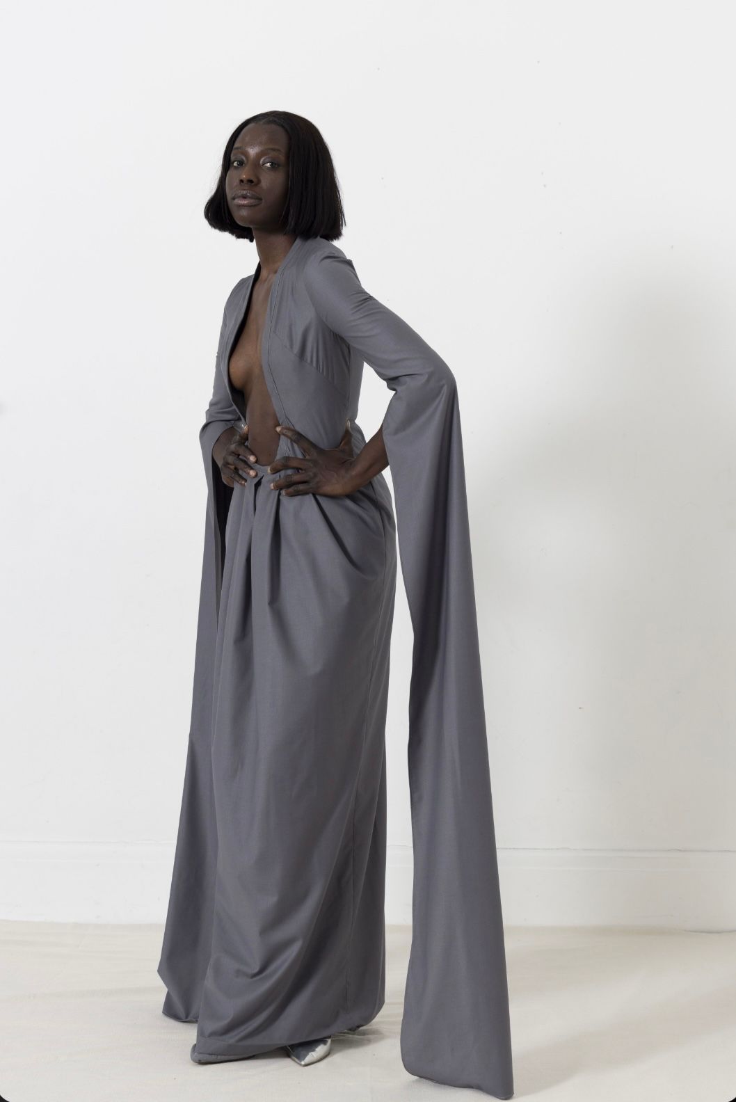 Woman in gray formal outfit with long sleeves poses against white background.