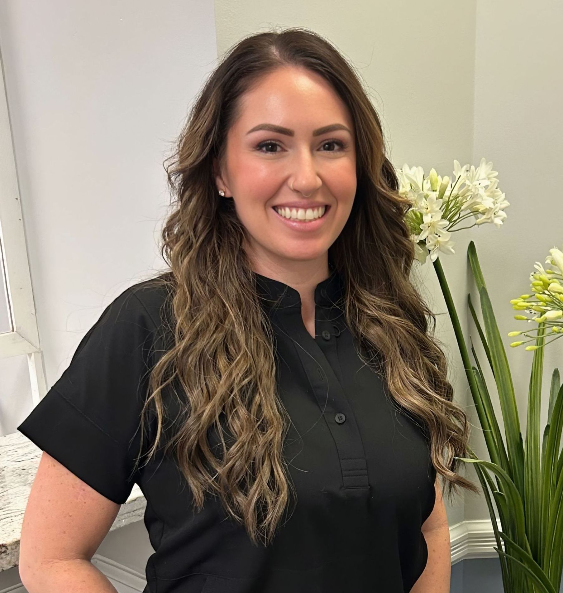 Woman smiling, wearing black shirt, near white flowers.