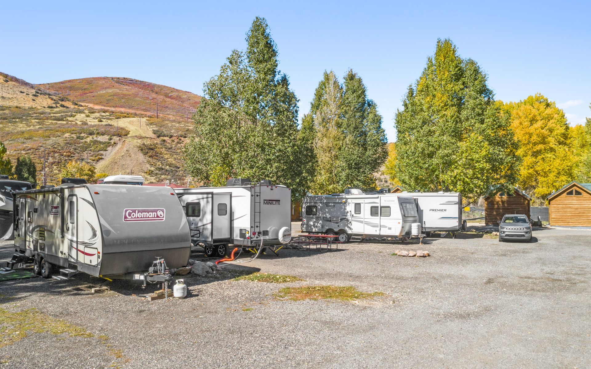 A row of rvs are parked in a gravel lot.