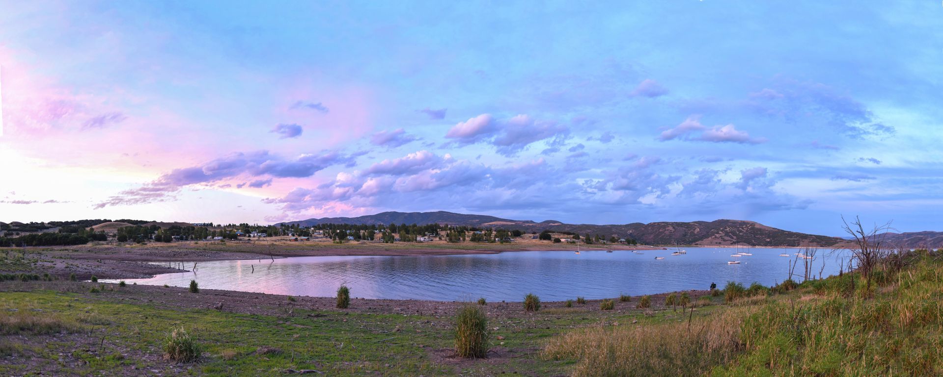 A large body of water surrounded by grass and trees with a sunset in the background.