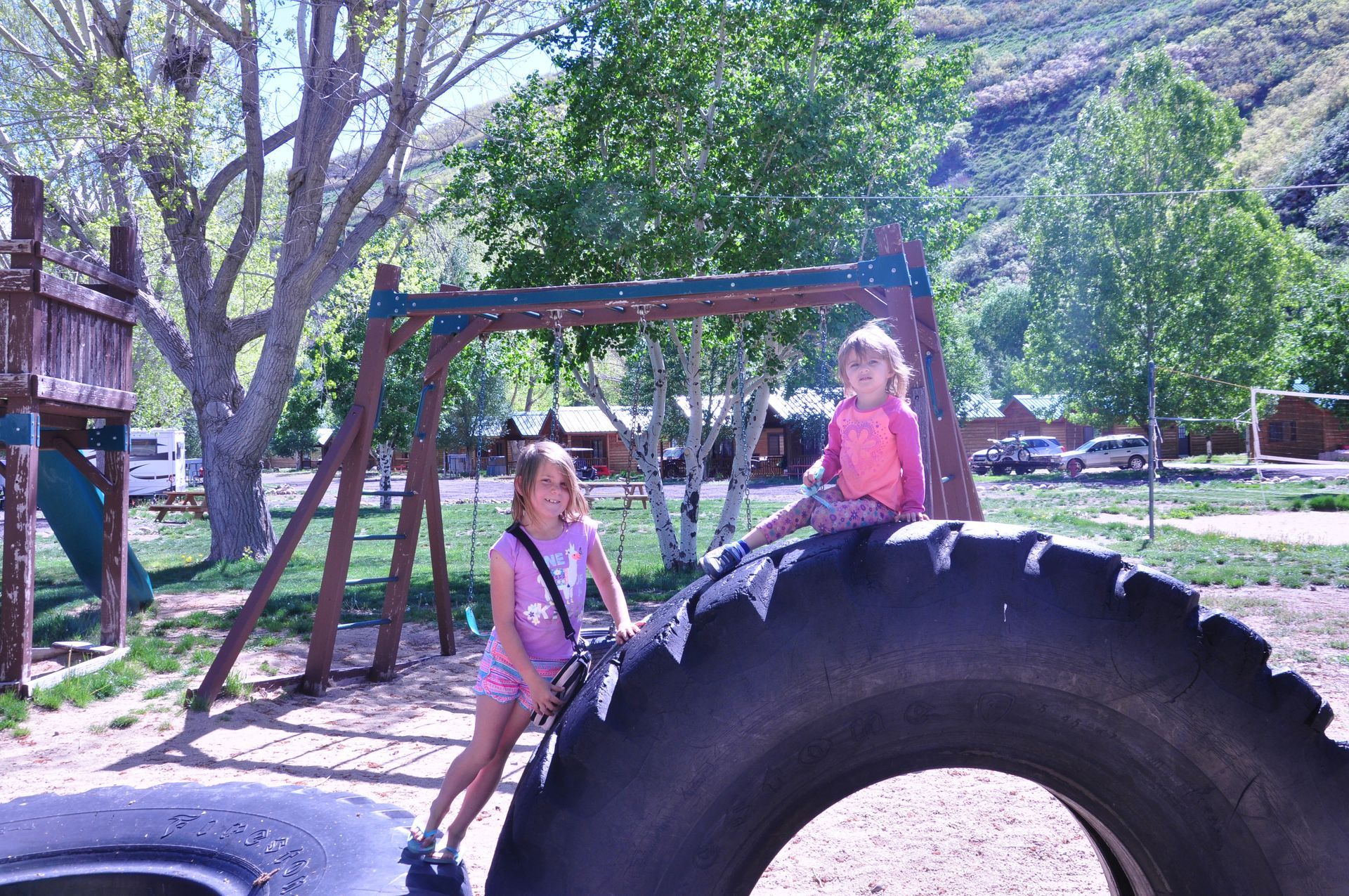 Two little girls are sitting on a tire at a playground.