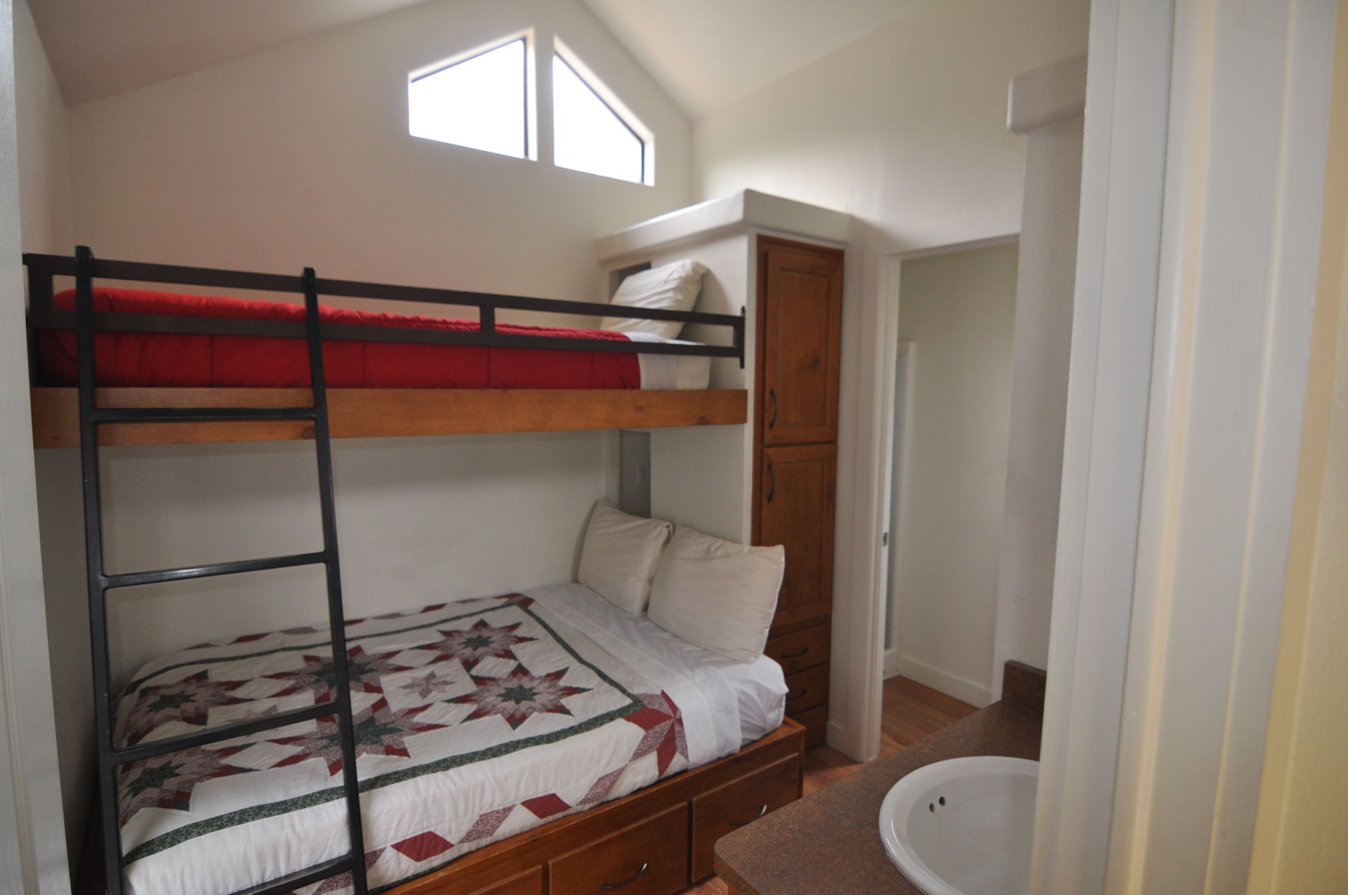 A bunk bed with a red blanket is in a room next to a bathroom.