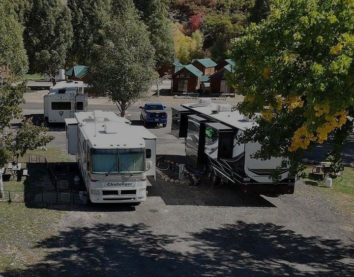 Full hookup RV sites at River's Edge RV Resort in Heber Valley, Utah, with large motorhomes parked among mature trees and mountain views