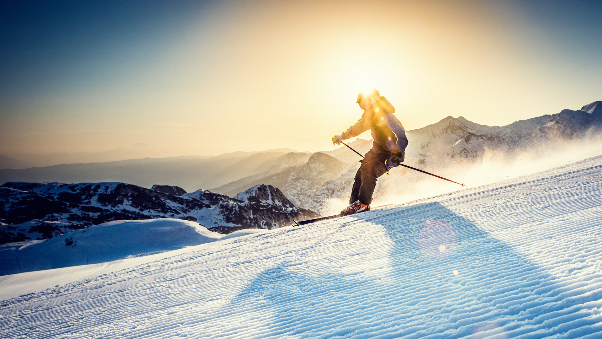 A man is skiing down a snow covered slope at sunset.