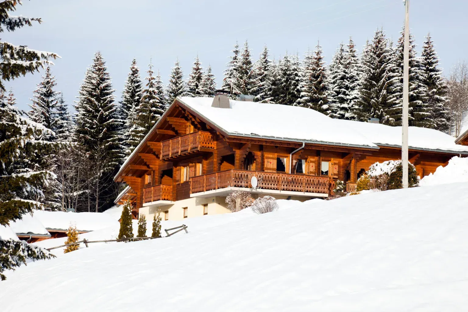 A large wooden house is sitting on top of a snow covered hill.