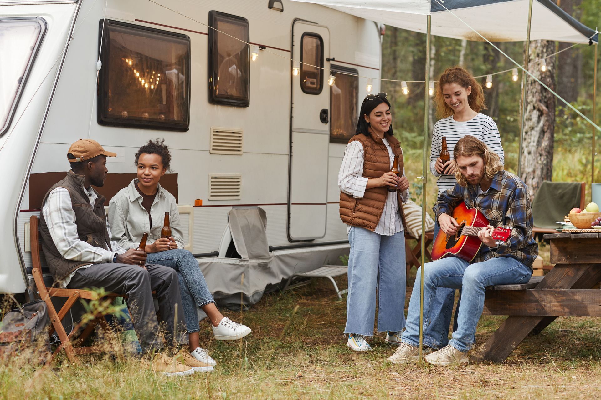 A group of people are sitting around a picnic table in front of a trailer.