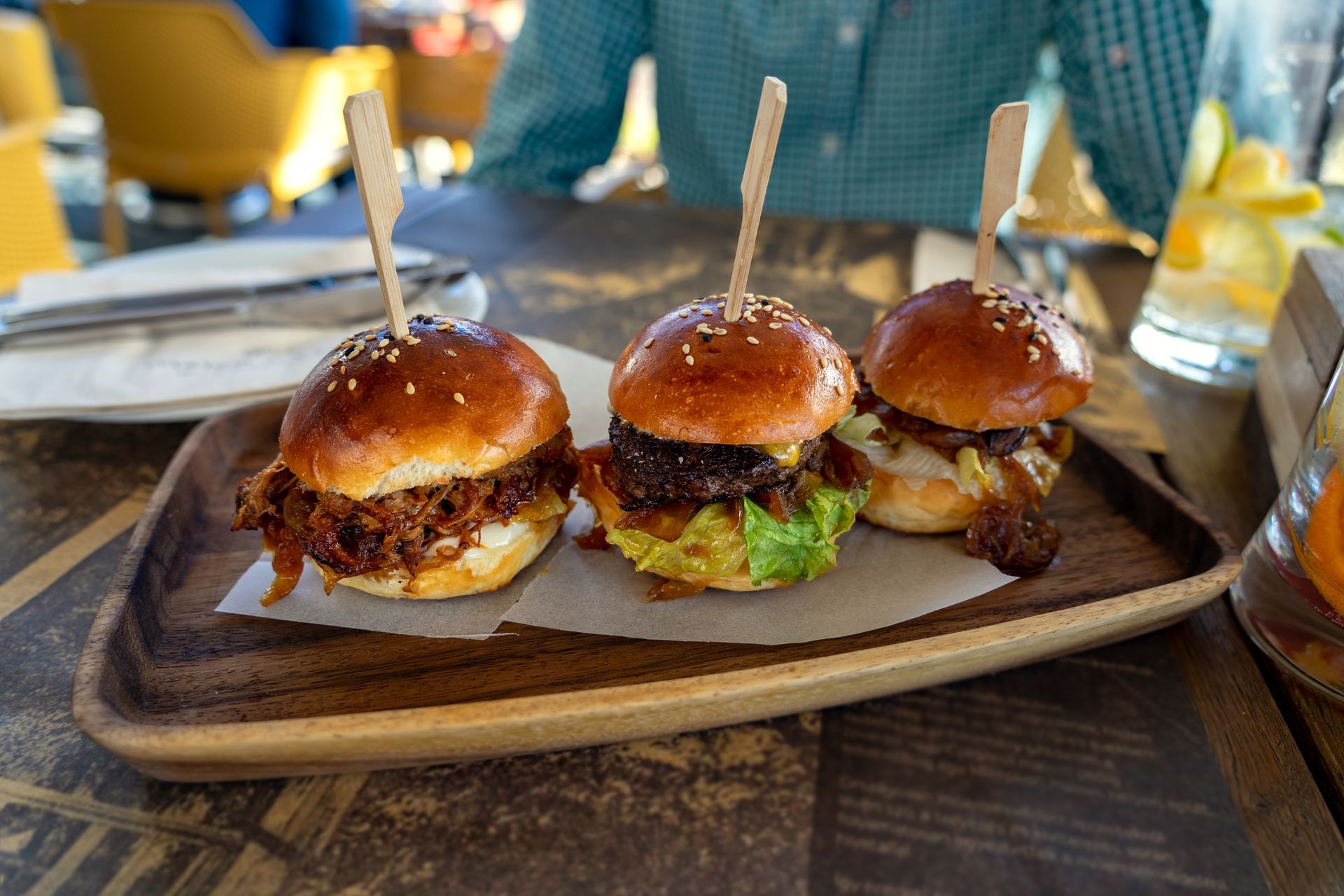 Three hamburgers are sitting on a wooden tray on a table.