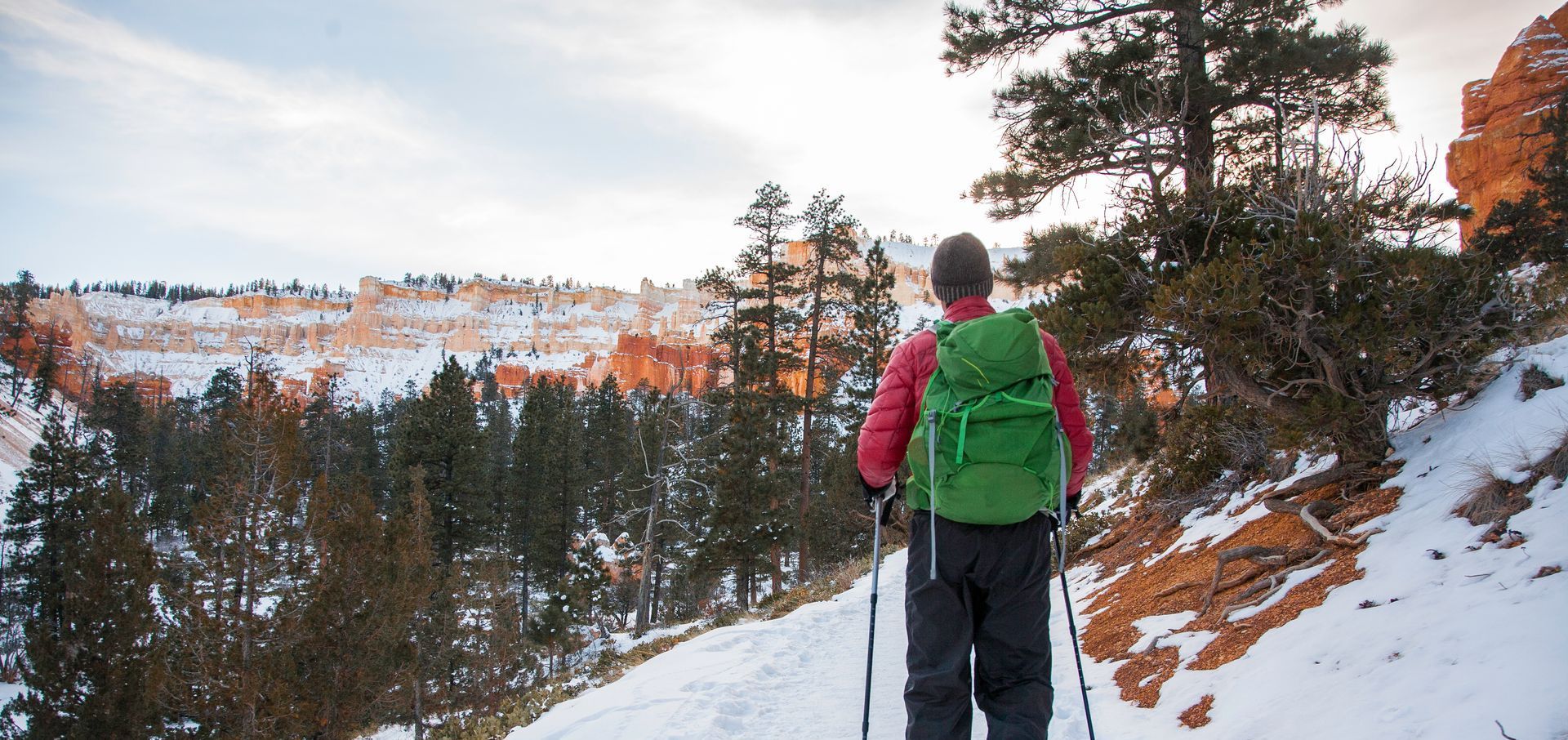 A person with a green backpack is hiking in the snow.