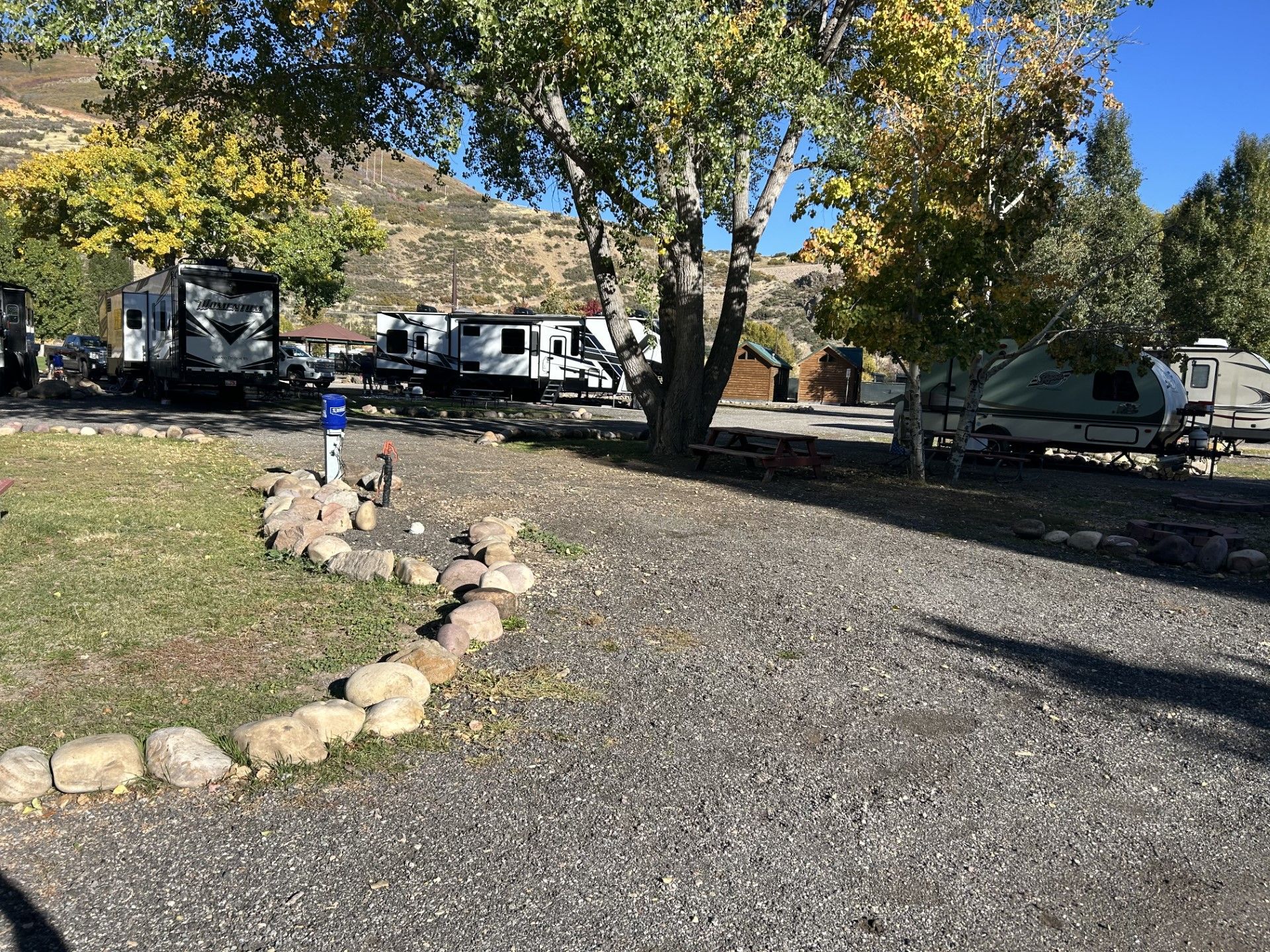 A group of rvs parked in a gravel lot next to trees.