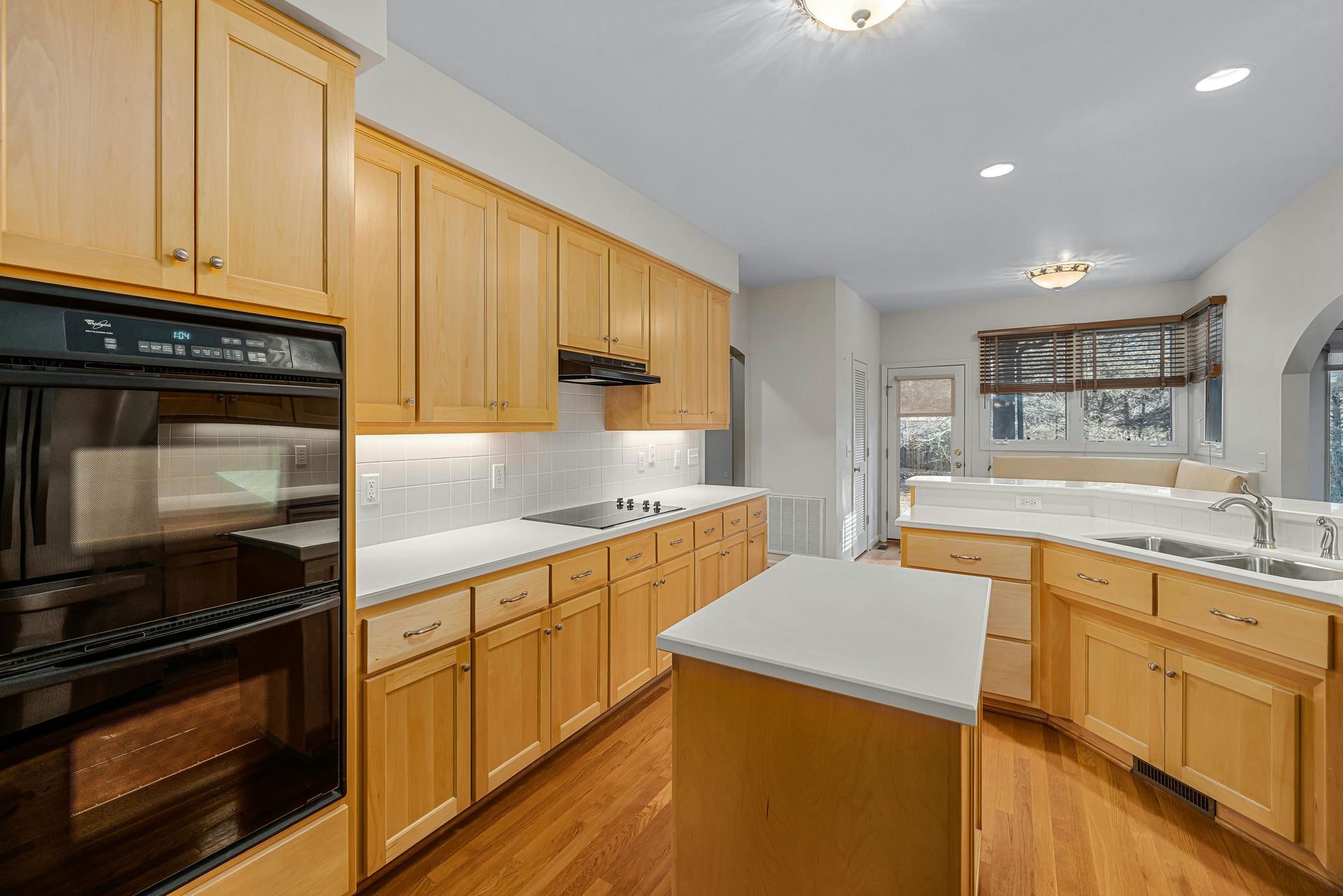 Modern kitchen with light wood cabinets, white countertops, a center island, and hardwood floors.