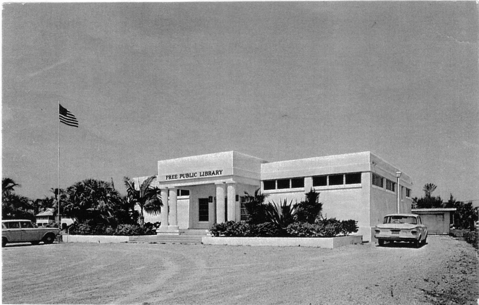 A black and white photo of a building with cars parked in front of it