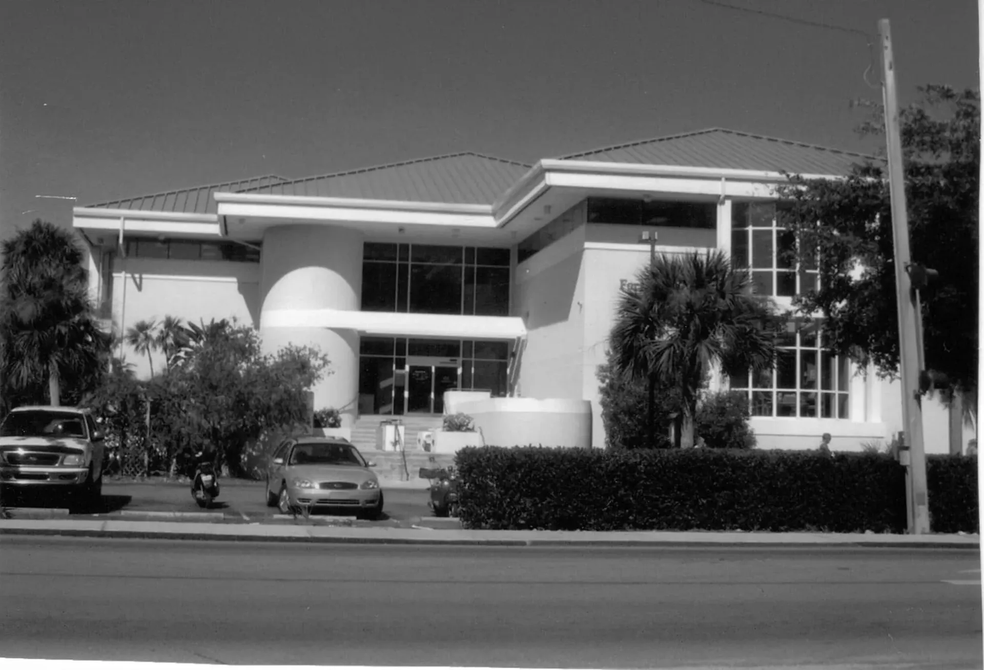 A black and white photo of a large white building with cars parked in front of it